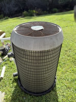 Old electric pool heater with visible rust and corrosion sitting on a lawn in Charlotte County, Florida — an example of a unit that needs replacement.